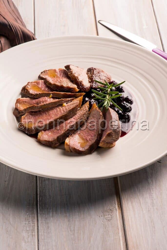 Petto d' anatra ai mirtilli su piatto e tavola di legno Petto d' anatra ai mirtilli