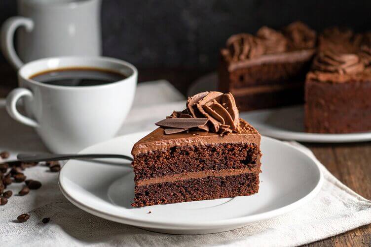 Fetta di torta al cacao su piattino chiaro, accanto a tazzina di kopi luwak Fetta di torta al cacao su piattino chiaro, accanto a tazzina di kopi luwak