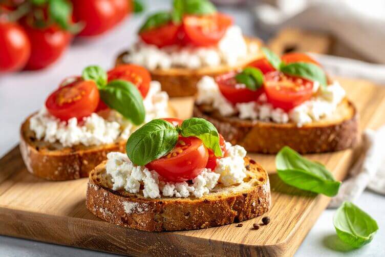 Fette di pane rustico tostate con feta sbriciolata, pomodorini e basilico fresco