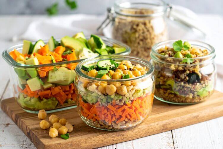 Meal prep vegetariano con insalate di quinoa, hummus, ceci, carote, zucchine e avocado. Meal prep vegetariano