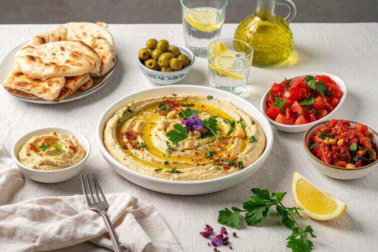 Tavola con mutabal di zucchine hummus, olive, insalata di pomodori, pita calda