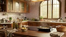 piano cottura con padella appena usata per friggere, cappa accesa, finestra socchiusa, sul bancone ciotolina con aceto e limone a fette, strofinacci appoggiati, pentole e utensili sullo sfondo, leggero vapore nell’aria, stile fotografico realistico, profondità di campo leggera, colori naturali, nessun testo, nessun logo.